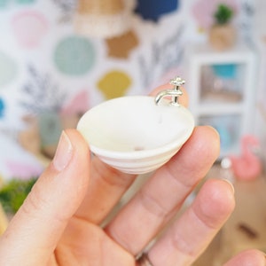 May include: A miniature white porcelain sink with a silver faucet. The sink is being held in a hand.