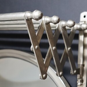May include: A silver metal wall-mounted towel rack with a folding design. The rack has multiple bars and is attached to a wall with screws.