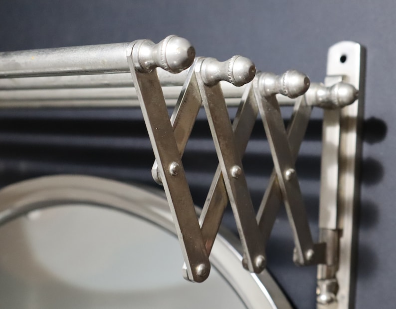May include: A silver metal wall-mounted towel rack with a folding design. The rack has multiple bars and is attached to a wall with screws.
