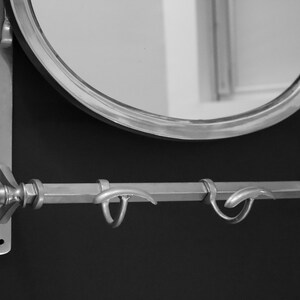 May include: A silver-toned wall-mounted mirror with a rounded oval shape and a decorative metal shelf with two hooks underneath.