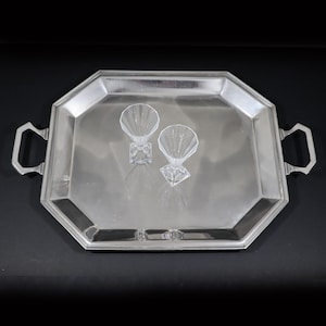 May include: A silver-toned, octagonal serving tray with two handles. Two clear, faceted glass cocktail glasses sit on the tray. The tray and glasses are on a black background.