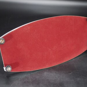 May include: A red velvet tray with a silver metal trim and four small, round feet. The tray has a curved, elongated shape and is designed to hold items. The velvet surface provides a soft contrast to the metal.