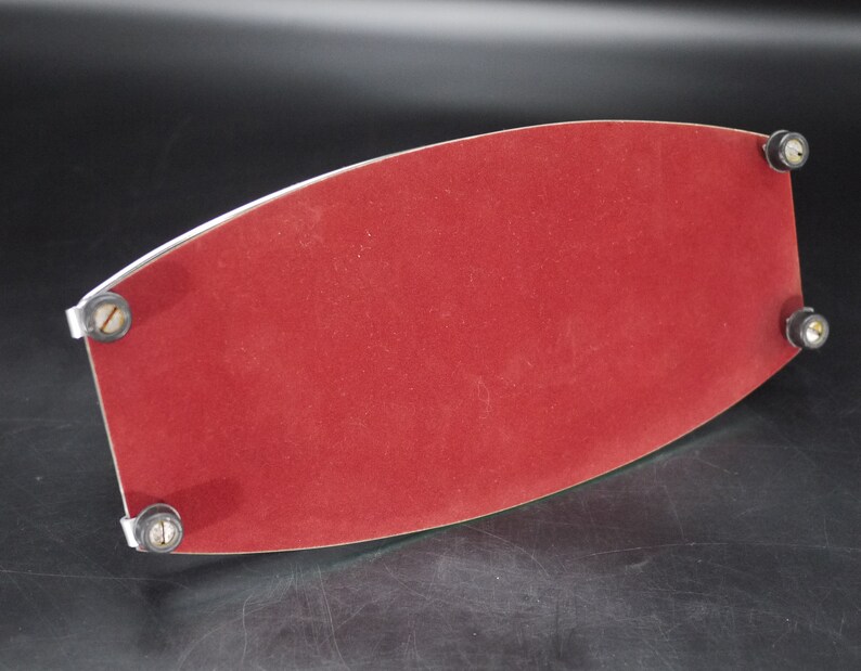 May include: A red velvet tray with a silver metal trim and four small, round feet. The tray has a curved, elongated shape and is designed to hold items. The velvet surface provides a soft contrast to the metal.