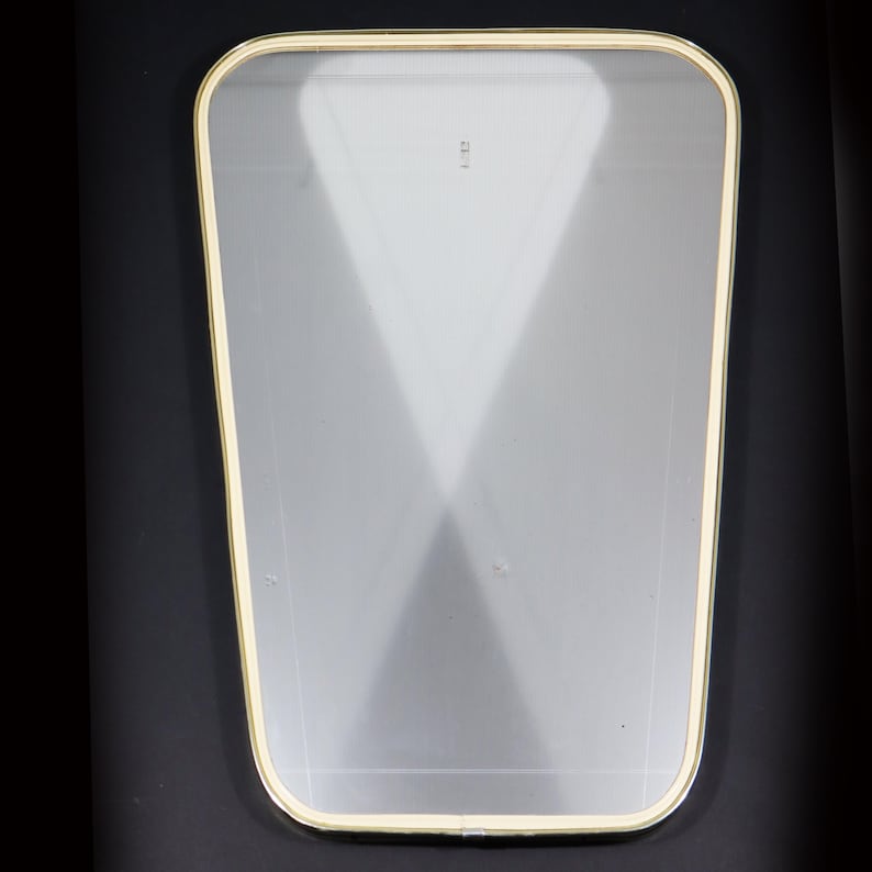 May include: A clear glass mirror with a gold-colored frame. The mirror has a slightly rounded shape and a beveled edge.