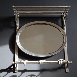 May include: A silver wall-mounted coat rack with a round mirror and three hooks. The rack has a decorative design with scrolls and curves.