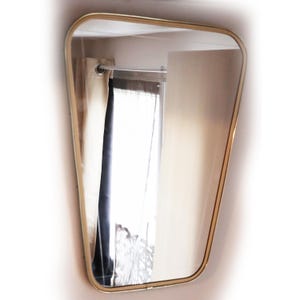 May include: A gold-framed, beveled-edge mirror with a slightly curved shape. The mirror reflects a room with curtains and a white ceiling.