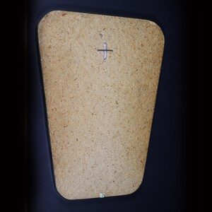 May include: A close-up of a light brown, rectangular, wooden mirror with a black frame. The mirror has a small, silver cross in the center.