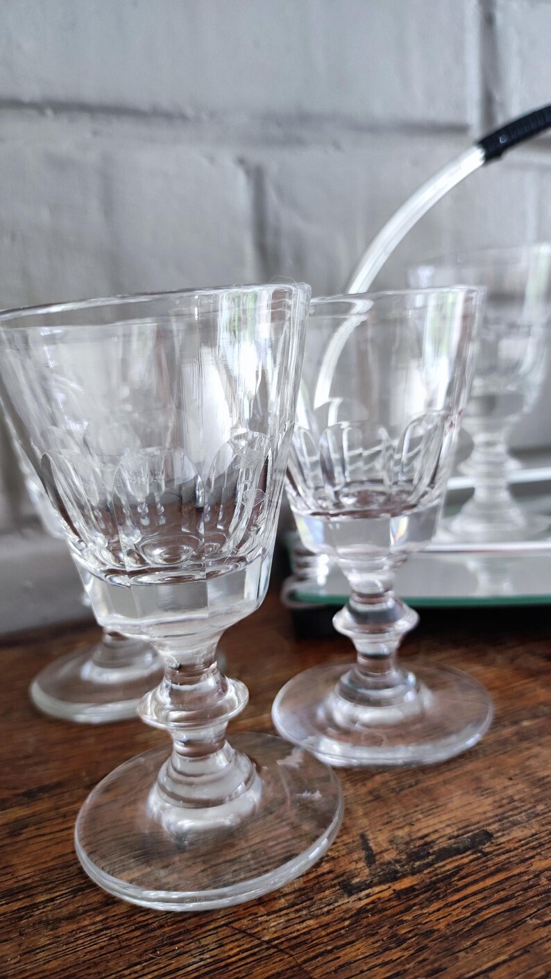 May include: Clear, stemmed glassware with etched designs. The glasses have a rounded bowl, a decorative stem, and a circular base. The glassware is likely for serving beverages. The glasses are on a wooden surface.