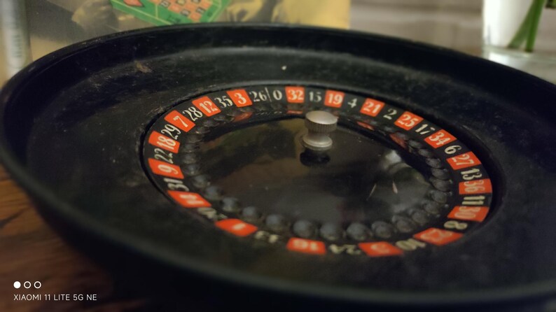 May include: A black roulette wheel featuring a central silver knob and a circular track with alternating red and black numbered segments. The numbers are printed in white, and the wheel includes a zero, with a smooth, dark, circular outer rim.