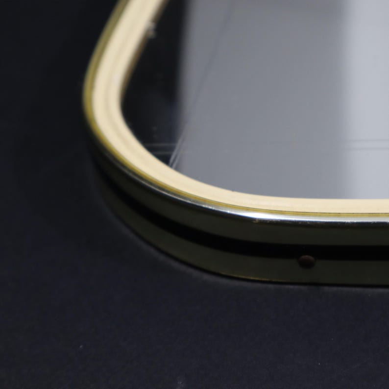 May include: Close-up of a gold-colored frame with a cream-colored border around a clear glass mirror.