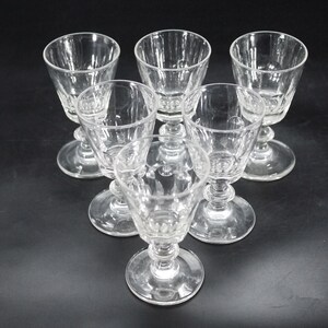 May include: Six clear, stemmed glasses arranged in a triangular pattern. Each glass features a detailed, textured design on the bowl and stem. The glasses are made of clear glass, reflecting light against a dark background. Ideal for serving beverages.