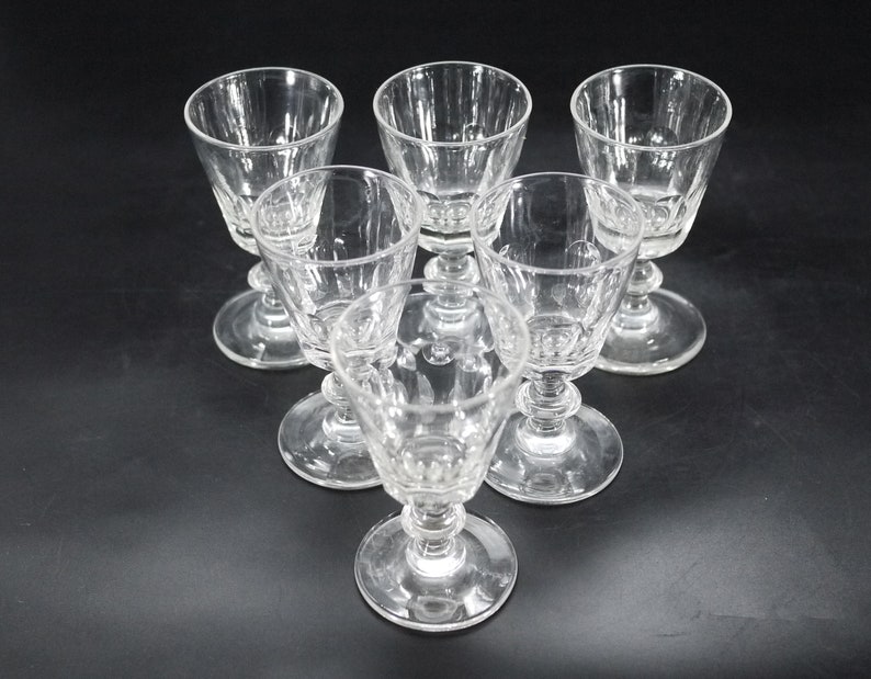 May include: Six clear, stemmed glasses arranged in a triangular pattern. Each glass features a detailed, textured design on the bowl and stem. The glasses are made of clear glass, reflecting light against a dark background. Ideal for serving beverages.