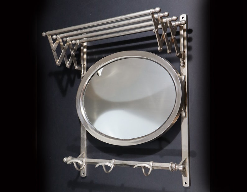 May include: A silver wall-mounted coat rack with a mirror and a fold-down towel rack. The rack has three hooks and a round mirror.