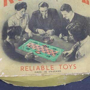 May include: A vintage cardboard game box featuring a black and white illustration of four people playing roulette around a green table. The text RELIABLE TOYS and MADE IN ENGLAND is printed in red and black at the bottom of the box cover.