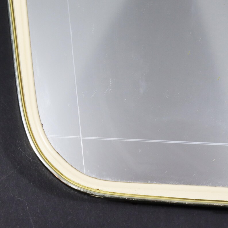 May include: Close-up of the corner of a rectangular mirror with a gold and cream frame.