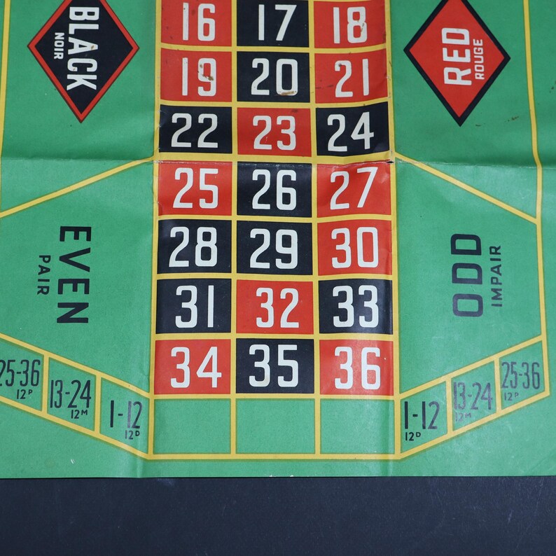 May include: A green roulette betting mat featuring a central grid of numbers from 16 to 36 in black and red squares. The mat includes text labels for Black, Red, Even, Odd, and betting sections for 1-12, 13-24, and 25-36 with yellow borders.