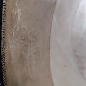 May include: The interior sweatband of a hat featuring a light beige leather lining with visible stitching along the edge. The text "LONDON" is clearly embossed on the material, accompanied by a faint, partially obscured brand name above it.
