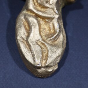 May include: Close-up of a gold-colored, abstract, organic-shaped sculpture. The sculpture has a smooth, textured surface and appears to be made of metal.