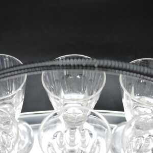 May include: A set of clear crystal glasses with a decorative beaded handle. The glasses are arranged on a silver tray, with a dark background. The glasses have a classic design, perfect for serving beverages.