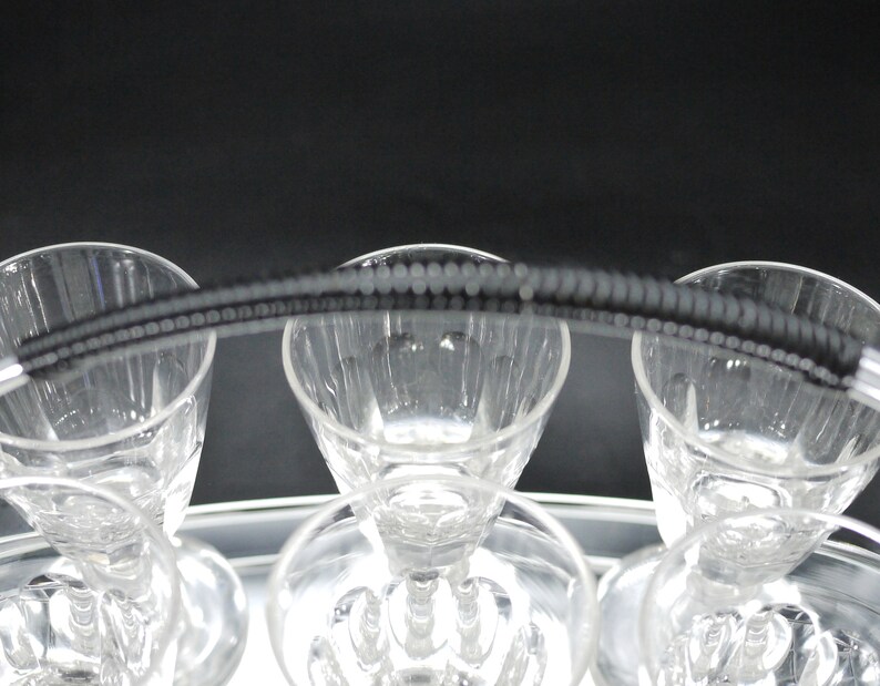 May include: A set of clear crystal glasses with a decorative beaded handle. The glasses are arranged on a silver tray, with a dark background. The glasses have a classic design, perfect for serving beverages.