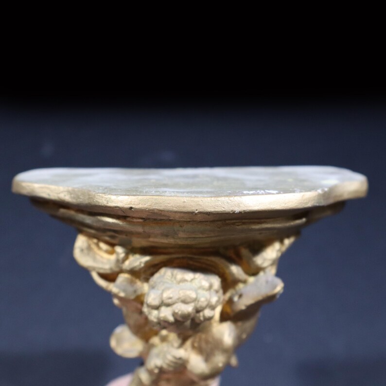 May include: A gold-colored decorative shelf with an ornate design. The shelf is shaped like a half-circle and has a raised edge. The shelf is supported by a sculpted figure.