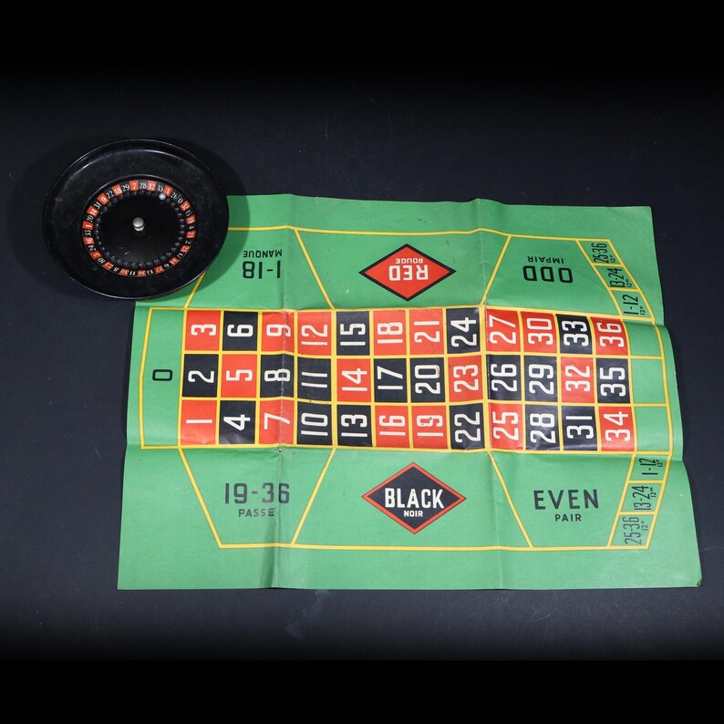 May include: A black roulette wheel with a silver center pin and a green felt betting mat featuring a grid of numbers from 0 to 36, with red and black squares, and text labels including Red, Black, Odd, Even, 1-18, and 19-36 in white and black.