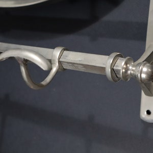 May include: A silver metal towel bar with a hook on the left side and a decorative finial on the right side. The bar is mounted to a wall.