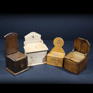 May include: Four wooden salt boxes in different styles. The boxes are in shades of brown and natural wood. Two have chair-like backs, one has a decorative wheel design, and another is a simple box with a lid. Each box has a unique design.