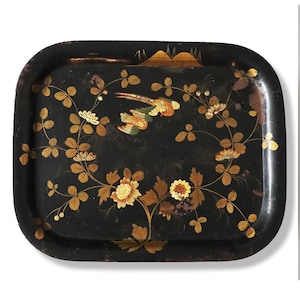 May include: Black rectangular serving tray with rounded corners, featuring a floral and bird design. The tray has a black background with gold and yellow flowers, leaves, and a bird. The tray's edges are slightly worn.