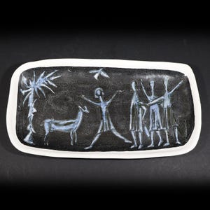 Könnte beinhalten: Rechteckige Servierplatte aus Keramik mit weißem Rand und schwarzem Innenraum. Der Innenraum zeigt ein stilisiertes Design von Figuren, einem Hirsch und einer Palme in Blau- und Weißtönen. Das Tablett ist wahrscheinlich für dekorative Zwecke.