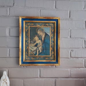 Peut inclure: Tableau religieux encadré représentant la Vierge à l'Enfant. Le cadre rectangulaire a une bordure bleue et des détails dorés. L'image montre la Vierge en robe bleue tenant l'enfant, avec un livre ouvert.