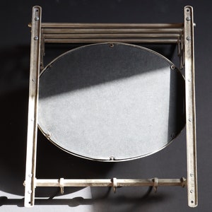 May include: A silver metal wall-mounted mirror with a round mirror and a shelf with hooks underneath.