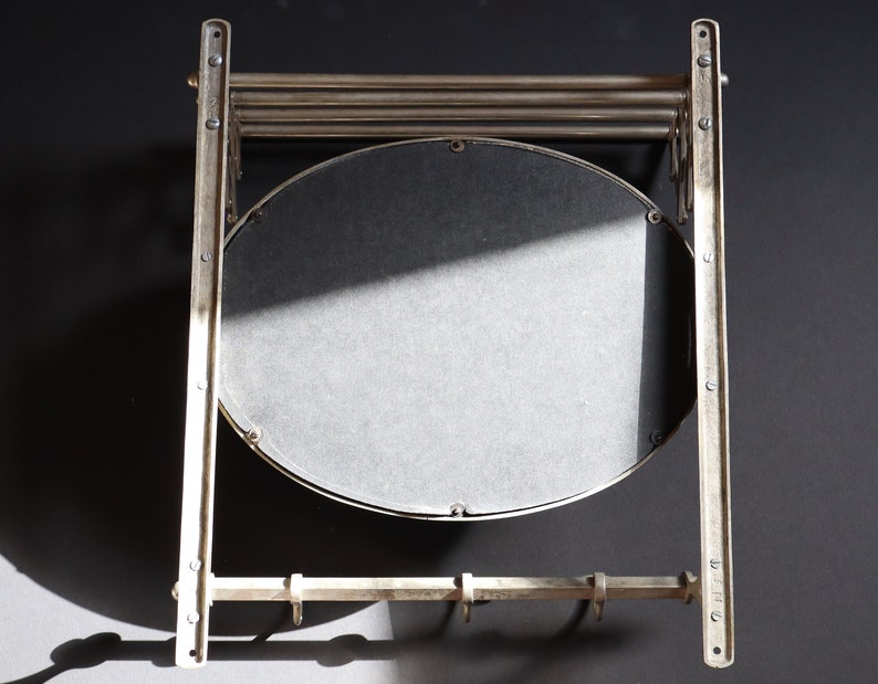 May include: A silver metal wall-mounted mirror with a round mirror and a shelf with hooks underneath.