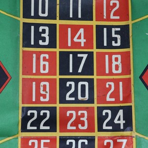 May include: A roulette game mat featuring a grid of numbered squares in black and red with white numerals. The central section displays numbers 10 through 24 arranged in three columns, bordered by green sections with thin yellow lines and red diamond shapes.