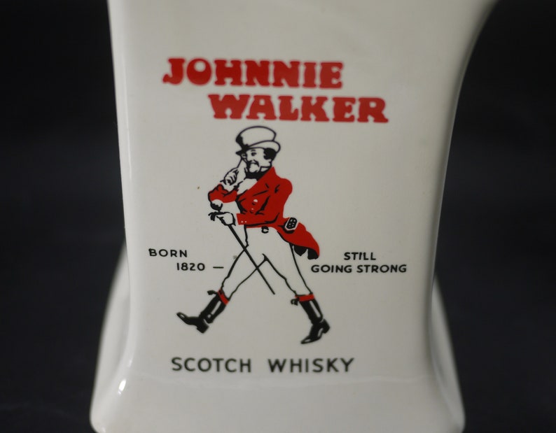 May include: White ceramic bottle with the "Johnnie Walker" logo in red. The logo features a man in a red coat and black boots, walking with a cane. The text "Born 1820" and "Scotch Whisky" are also visible.