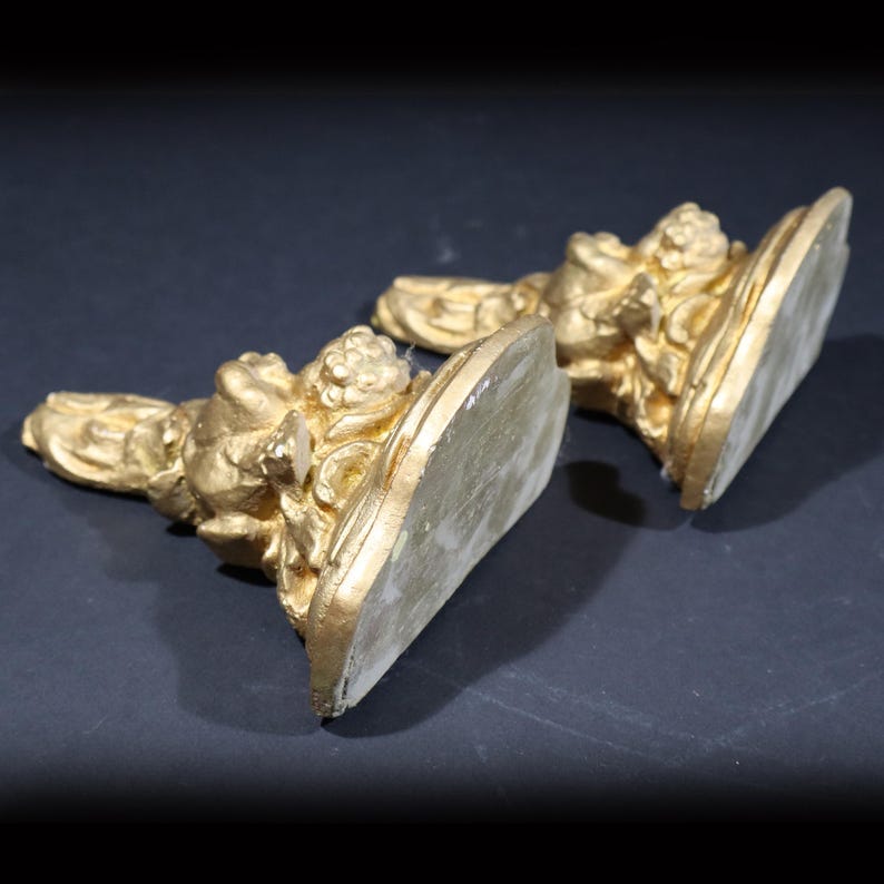 May include: A pair of gold-painted decorative bookends with a floral design. The bookends are made of a hard material and have a smooth, polished finish.