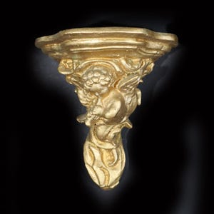 May include: A gold-colored wall shelf with an ornate design featuring a cherub figure. The shelf is made of plaster or resin and has a decorative, vintage style.