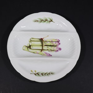 Peut inclure: Plat de service blanc divisé avec un bord festonné. Le plat présente une illustration peinte d'une botte d'asperges attachée avec un ruban rouge. Des asperges vertes et violettes sont au centre, avec des brins de verdure en haut et en bas.