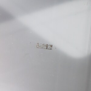 May include: A close-up of a light gray surface with a small, thin, silver scratch.