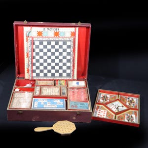 Peut inclure: Un ancien coffret de jeux rouge et marron avec un échiquier, diverses pièces de jeu et un éventail en bois. L'ensemble comprend une boîte avec le texte "LE TACTICIEN" et une boîte séparée avec des cartes à jouer. L'ensemble est ouvert, révélant le contenu.