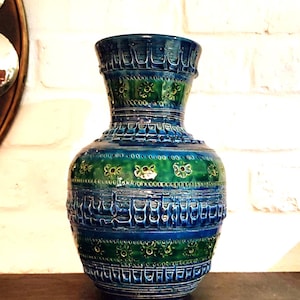 Peut inclure: Un vase en céramique avec une glaçure brillante dans des tons bleu profond et vert forêt. La surface est ornée de bandes horizontales de motifs géométriques en relief et de petites fleurs, créant un aspect texturé sur tout le corps.