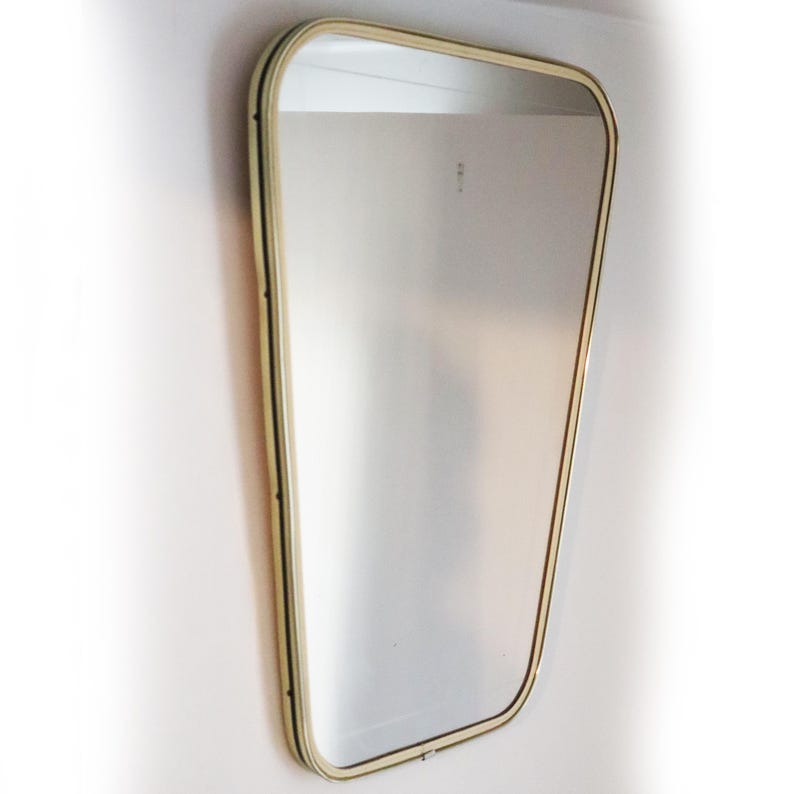 May include: A large, gold-framed mirror with a slightly curved, rectangular shape. The mirror is hanging on a white wall.