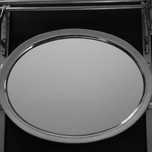 May include: A round, silver-framed mirror with a smooth, reflective surface. The mirror is attached to a metal stand with a swivel arm.