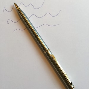 May include: A silver pen with a gold trim and the word "Lamy" engraved on the side.