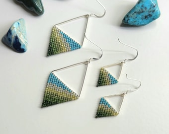 May include: A pair of triangle-shaped earrings with green, blue, and white beaded designs. The earrings are made with silver wire and have a simple hook closure.