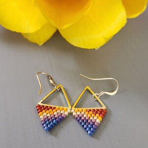 May include: A pair of triangle-shaped earrings with a rainbow color pattern. The earrings are made of small beads and have silver hooks.