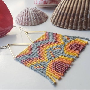 May include: A pair of gold triangle earrings with a fringe of colorful beads. The beads are in shades of gray, yellow, orange, and red, creating a geometric pattern.