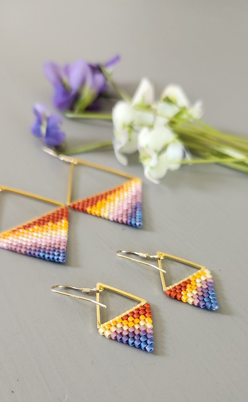 May include: A pair of gold triangle earrings with a rainbow gradient of beads. The earrings are made with small, colorful beads and have a geometric shape.