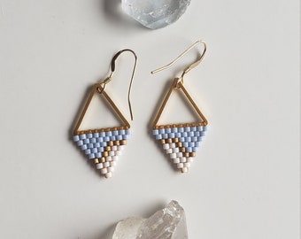 May include: A pair of gold triangle earrings with blue, white, and gold beaded fringe.
