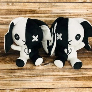 May include: Two plush bunny toys, each split vertically in black and white. The black side has a button eye and a white cross. The white side has a button eye and a white cross. A broken heart is embroidered on the chest.